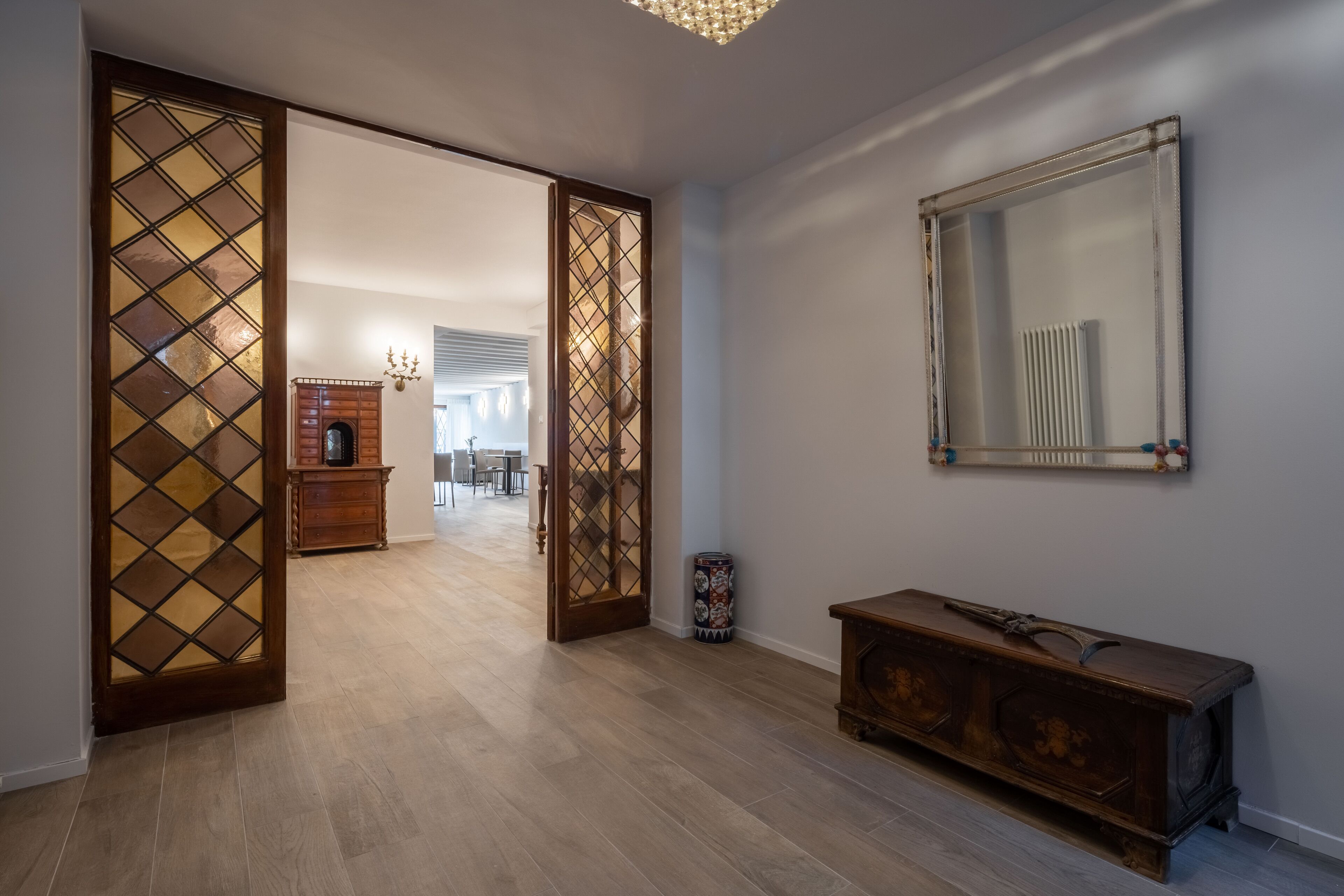 Um corredor com piso de madeira, um armário de madeira, um espelho na parede e uma porta com painel de vidro decorativo.