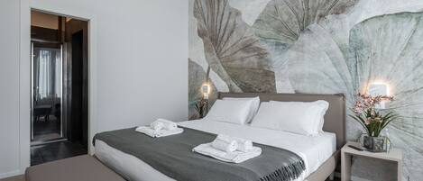 A modern bedroom with a large bed, a bench, a nightstand with a plant, and a wall with a leaf mural.