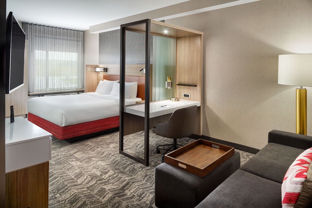A hotel room with a bed, desk, chair, and a small seating area.