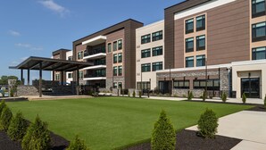 A modern multi-story hotel with a covered entrance, landscaped grounds, and a clear sky.