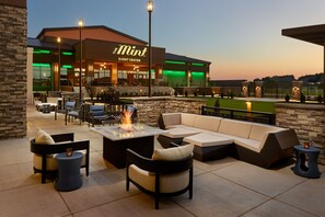 An outdoor seating area with a fire feature, stone walls, and a building labeled "The Mint Event Center" in the background. - Springhill Suites By Marriott Franklin Mint (Franklin)