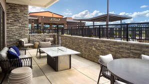An outdoor patio with a stone wall, a covered seating area, and a view of the event center in the background.