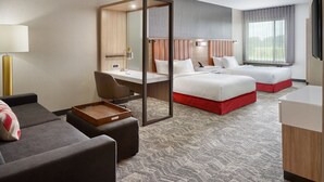 A hotel room with a desk, two beds, a sofa, and a TV.