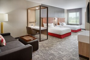 A hotel room with a desk, two beds, a sofa, and a TV.