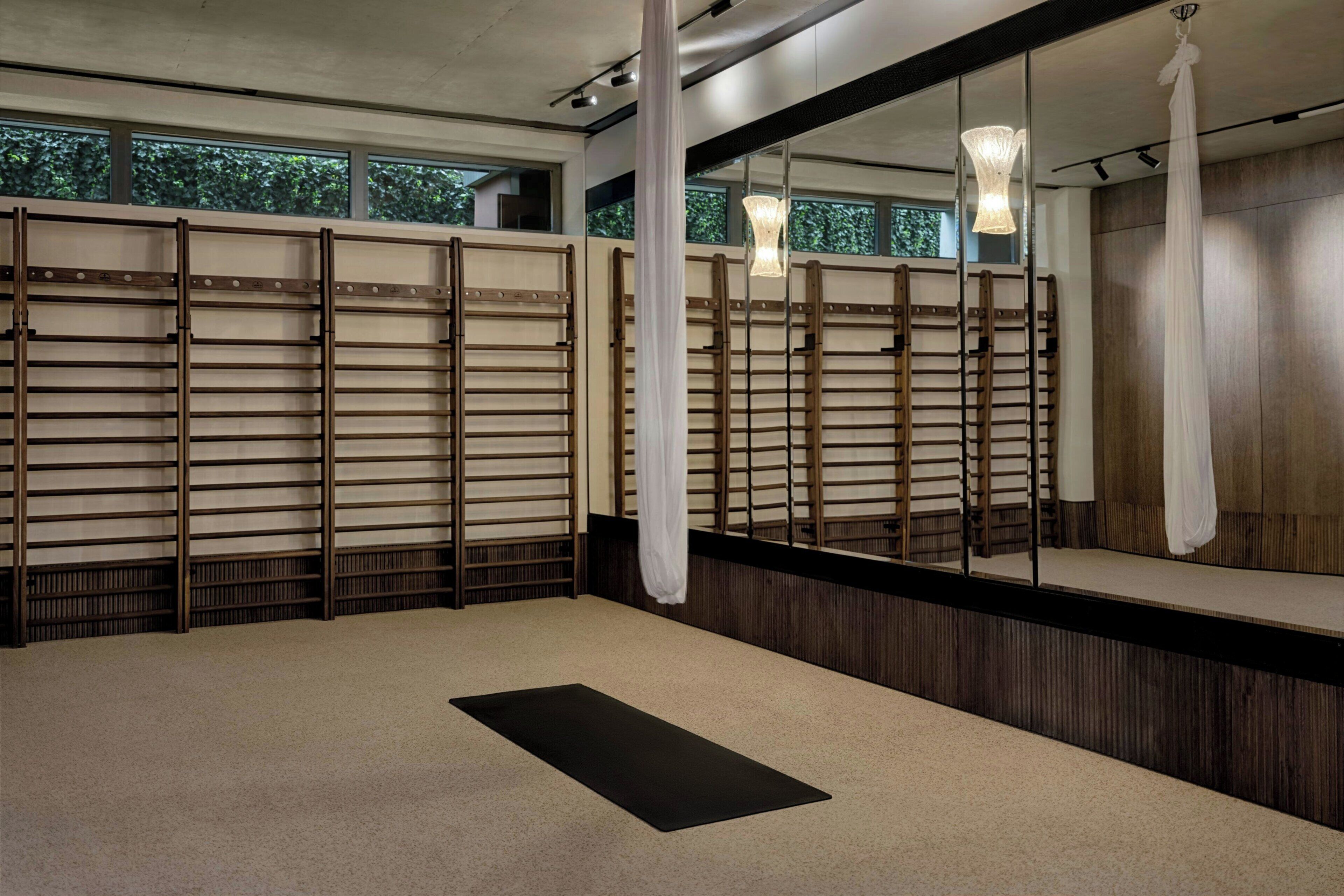 Une pièce dotée d’un grand miroir, de cloisons en lattes de bois, d’un tapis de yoga noir et d’un luminaire suspendu.