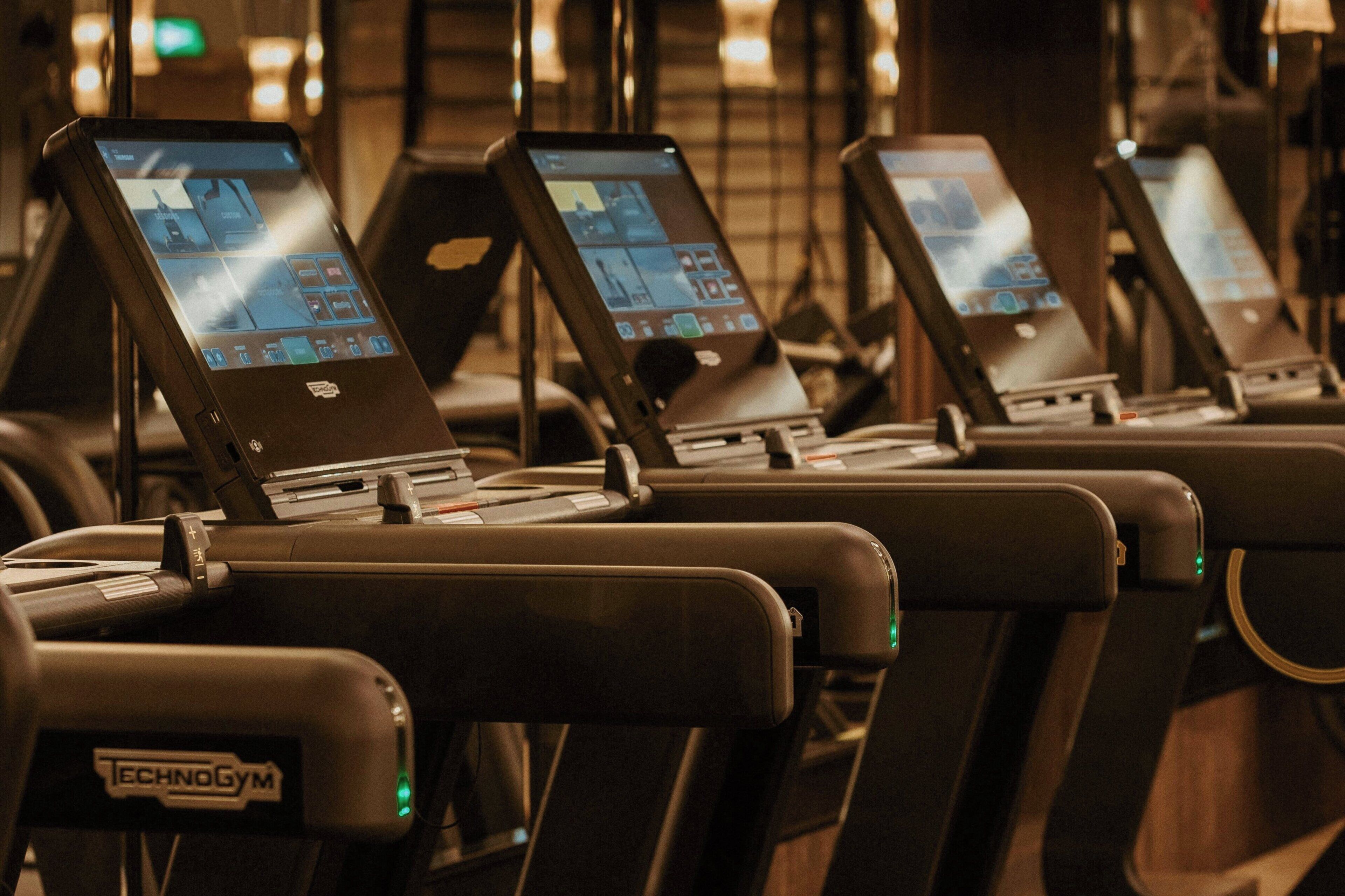 Una hilera de máquinas de ejercicio con pantallas digitales, probablemente en un gimnasio.