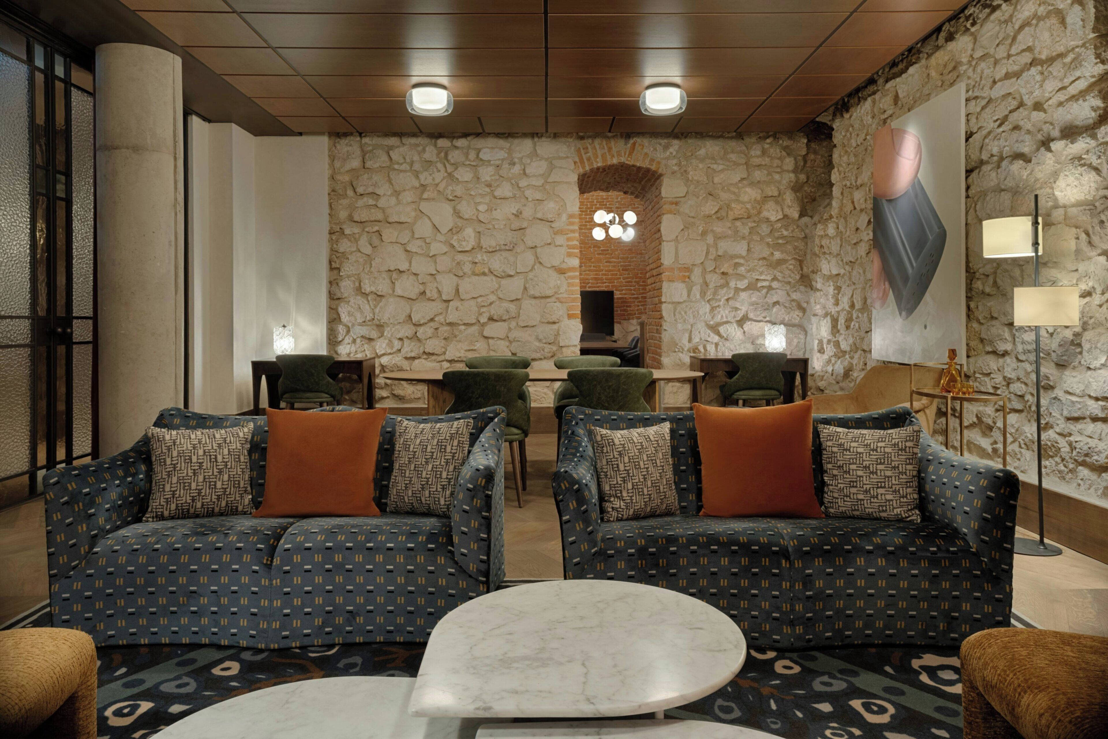 A modern lounge area with patterned sofas, a round coffee table, and a stone wall backdrop.