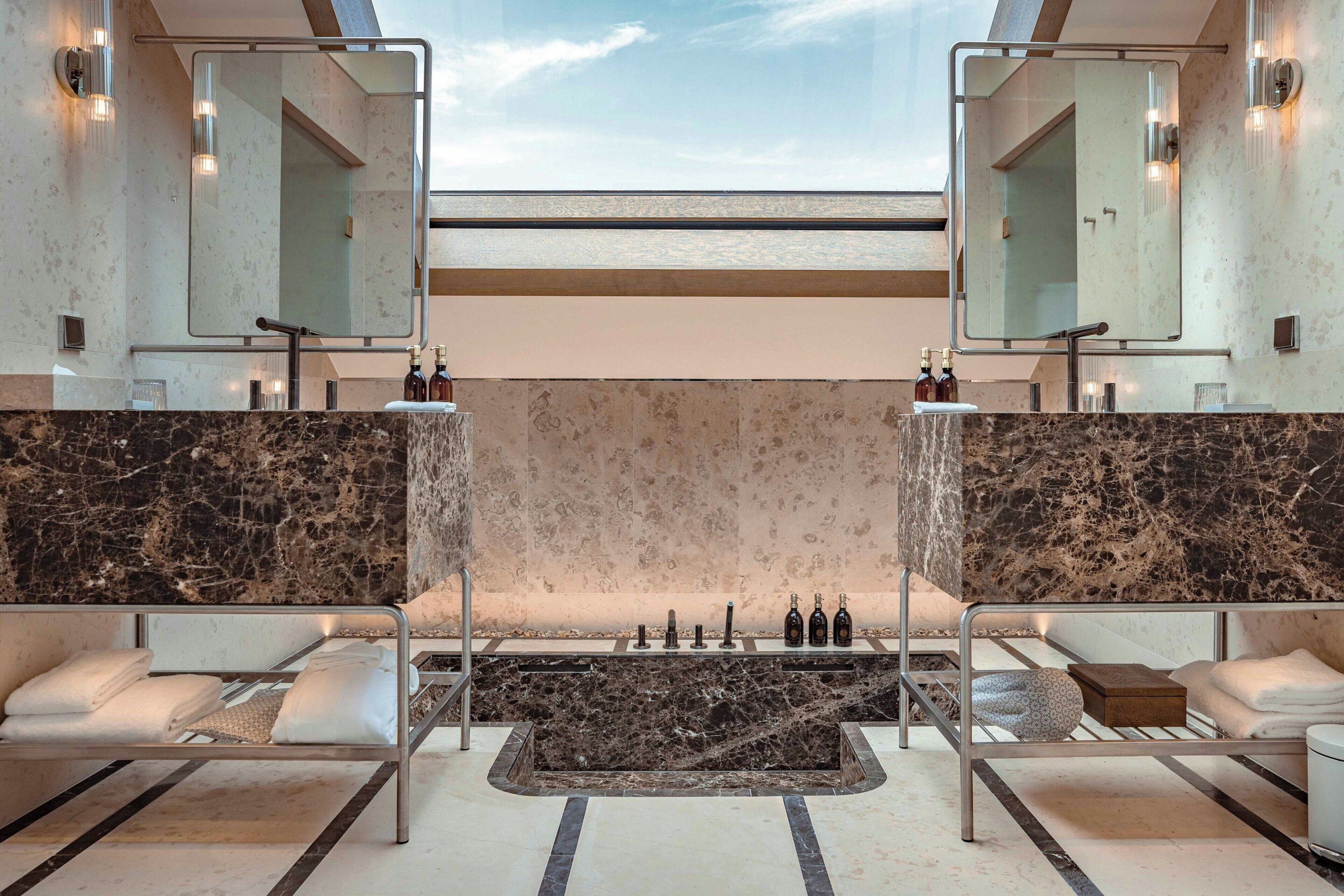 Een moderne spa met een centraal gelegen bubbelbad, twee zithoeken met handdoeken en grote spiegels.