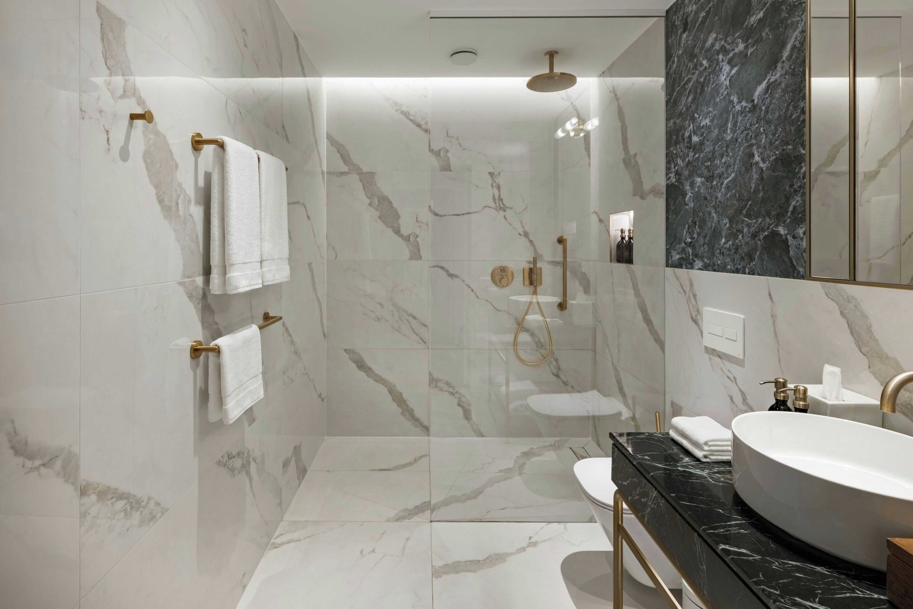 A modern bathroom with marble walls, a glass-enclosed shower, a black countertop, and a large mirror.