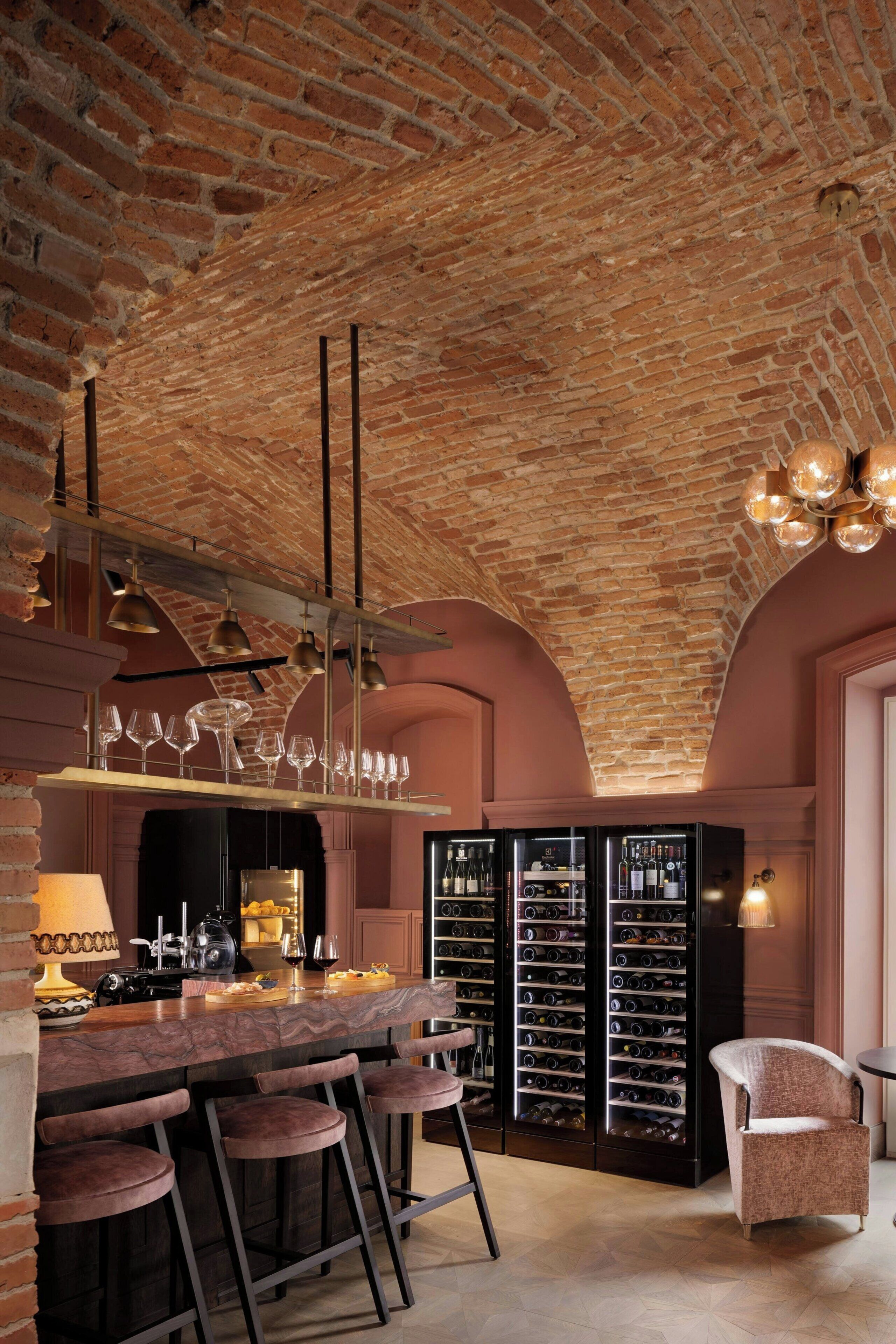 Een bar met bakstenen plafond, wijnrekken en barstoelen.