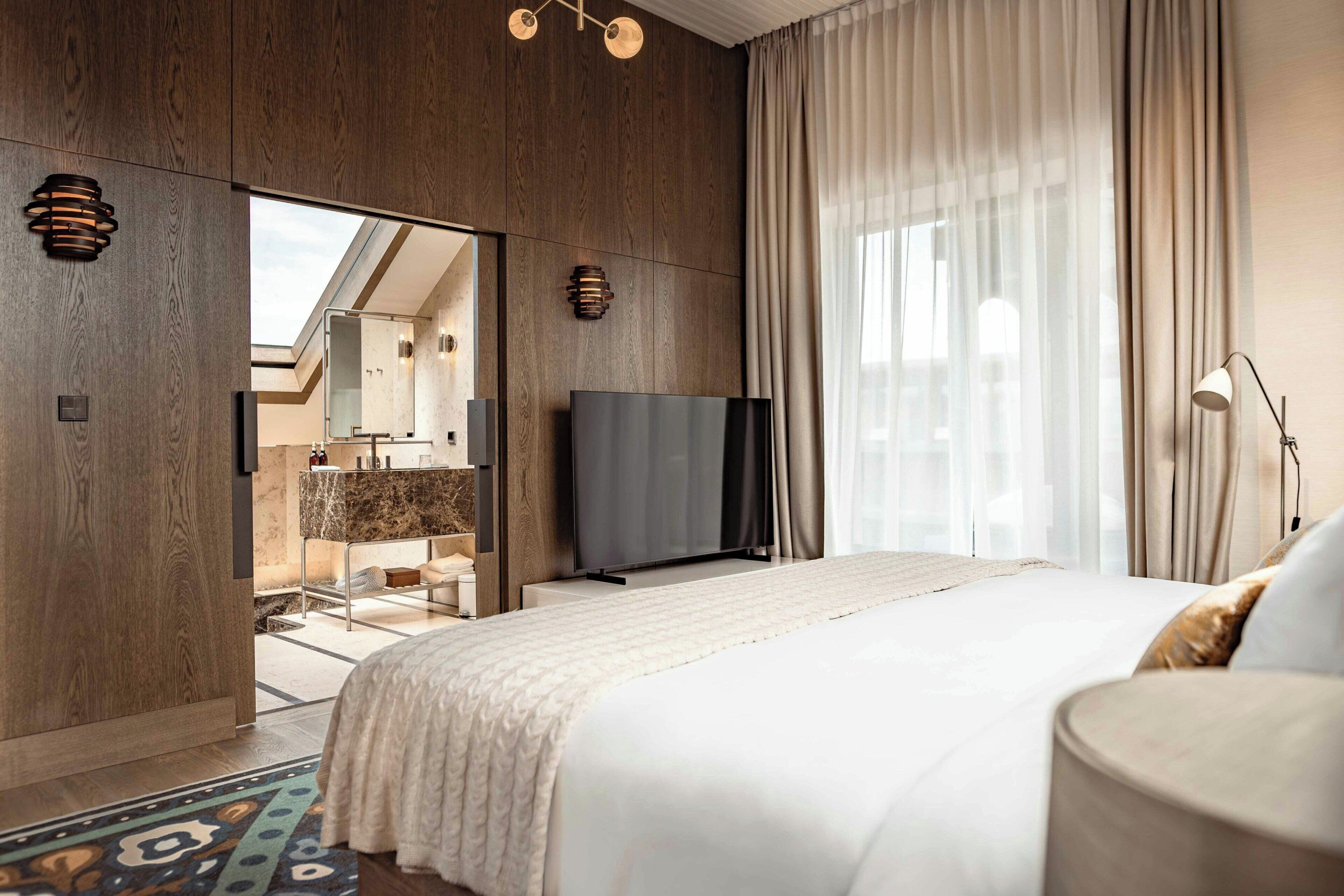 Een moderne hotelkamer met een groot bed, een flatscreen televisie, een inloopkast en uitzicht op het buitengebied.