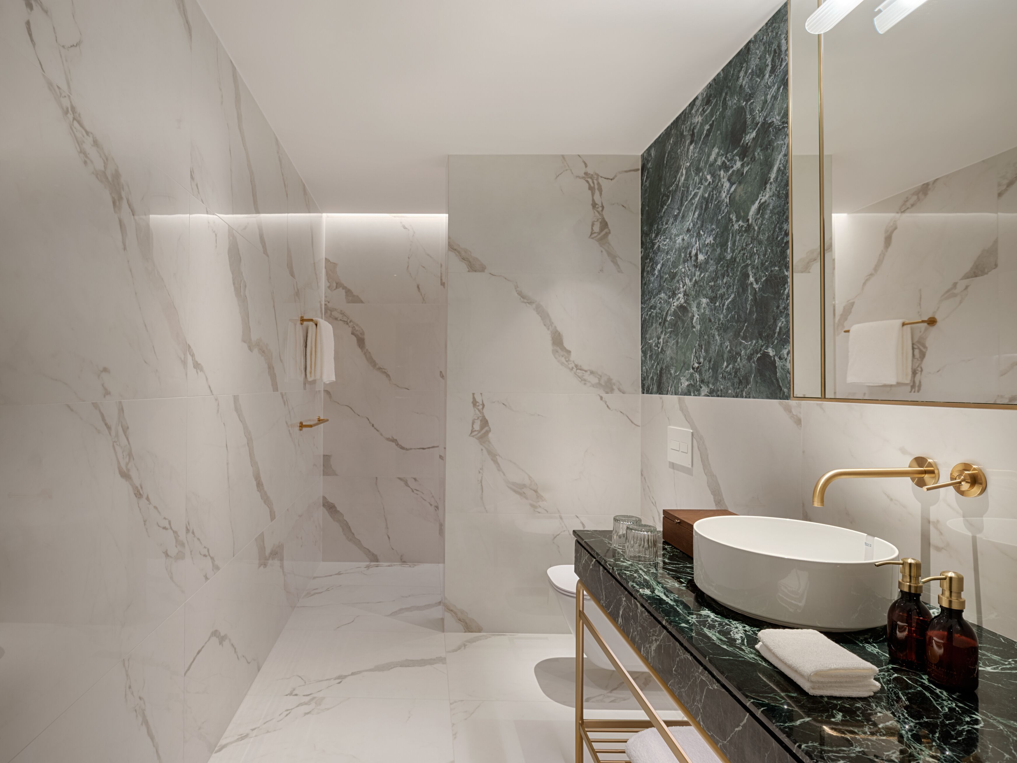 A modern bathroom with marble walls, a large sink, and a gold faucet.