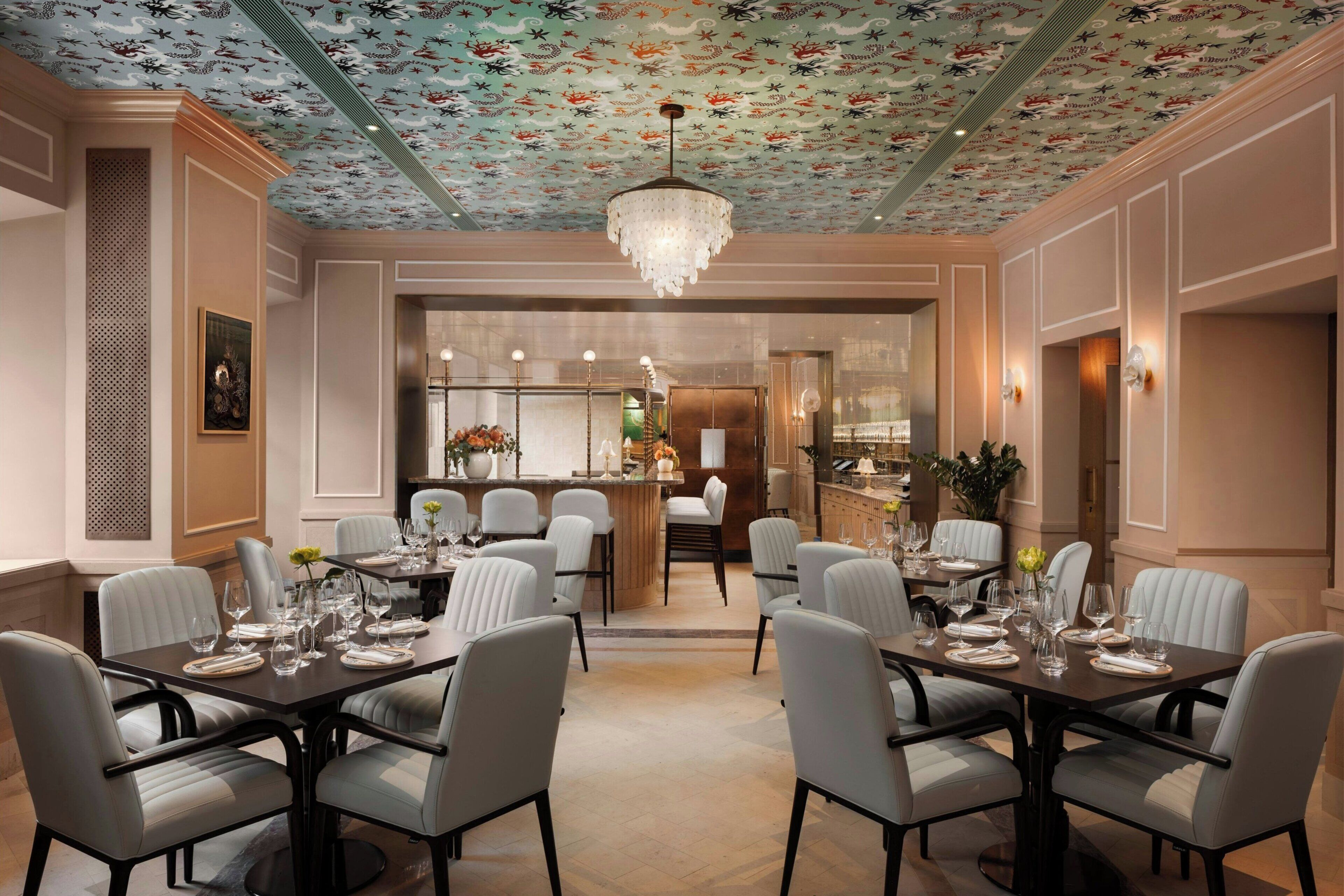 A dining area with a patterned ceiling, a chandelier, and a bar in the background.
