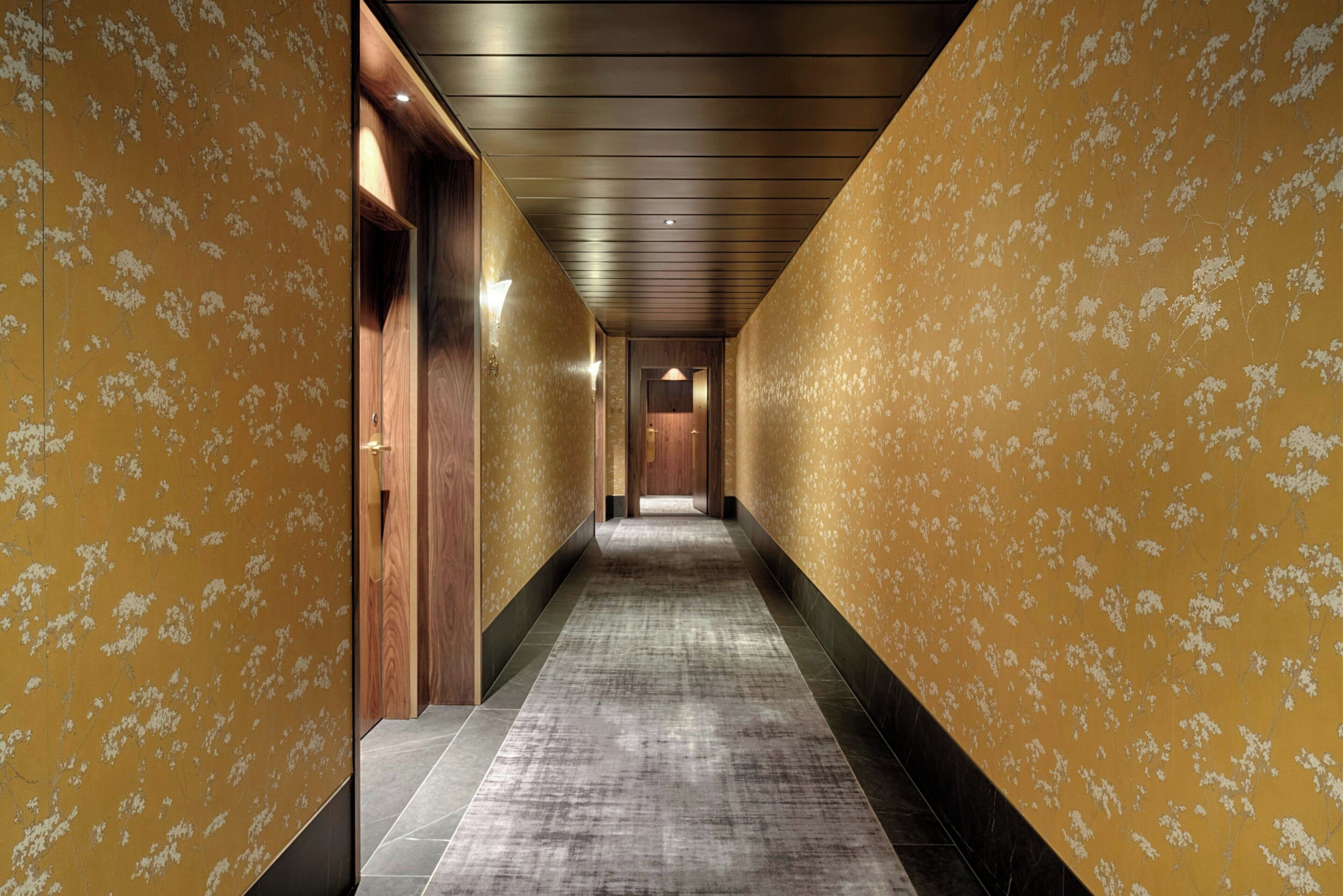 A hallway with patterned walls and a carpeted floor, leading to a door at the end.