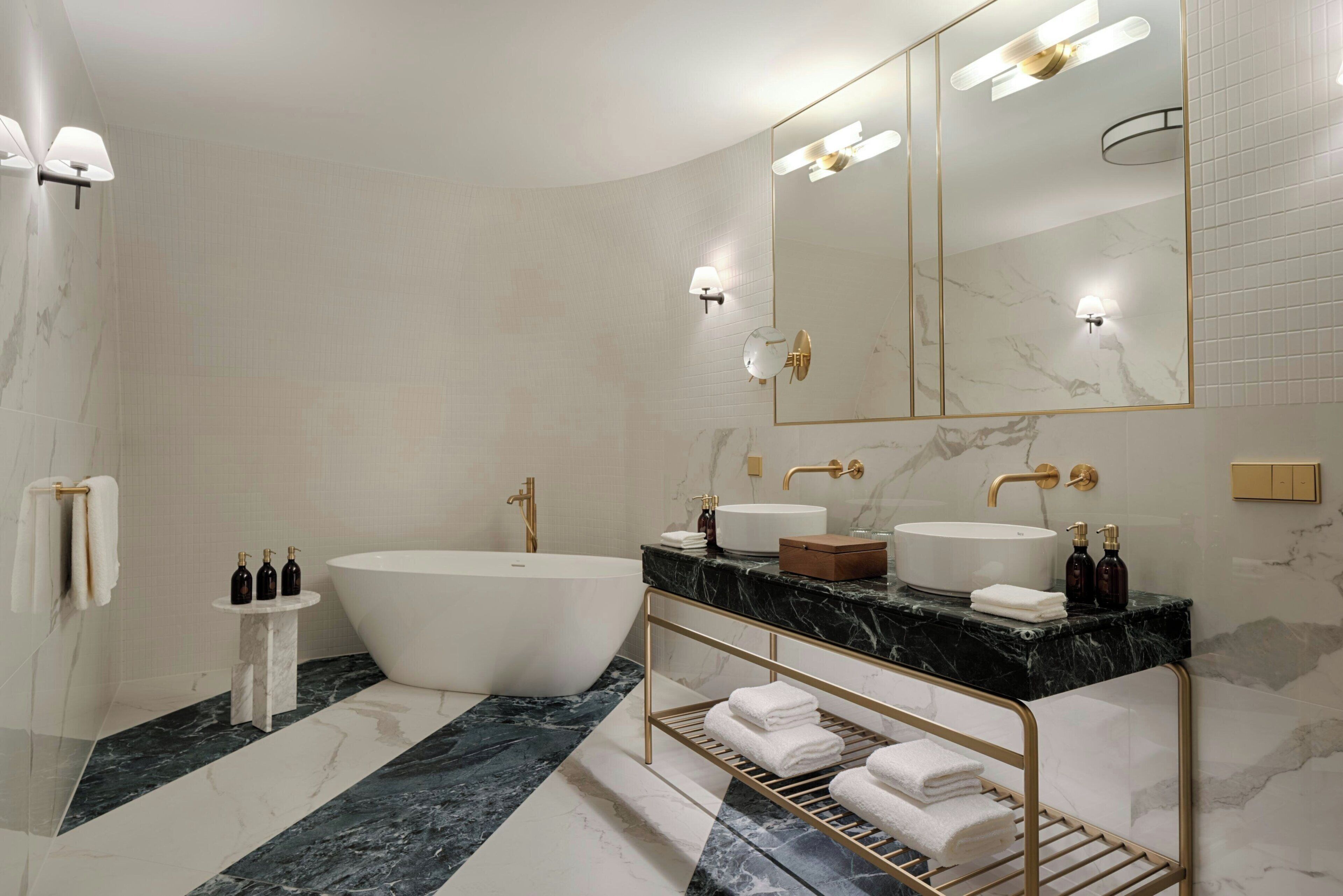 A modern bathroom with a freestanding bathtub, a vanity with a large mirror, and marble flooring.