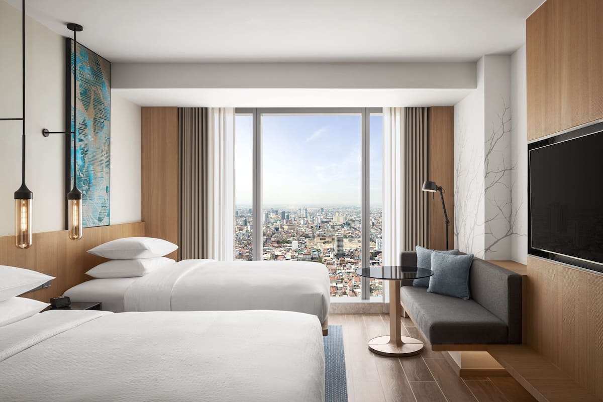 A hotel room with two beds, a sofa, a TV, and a large window with a city view.