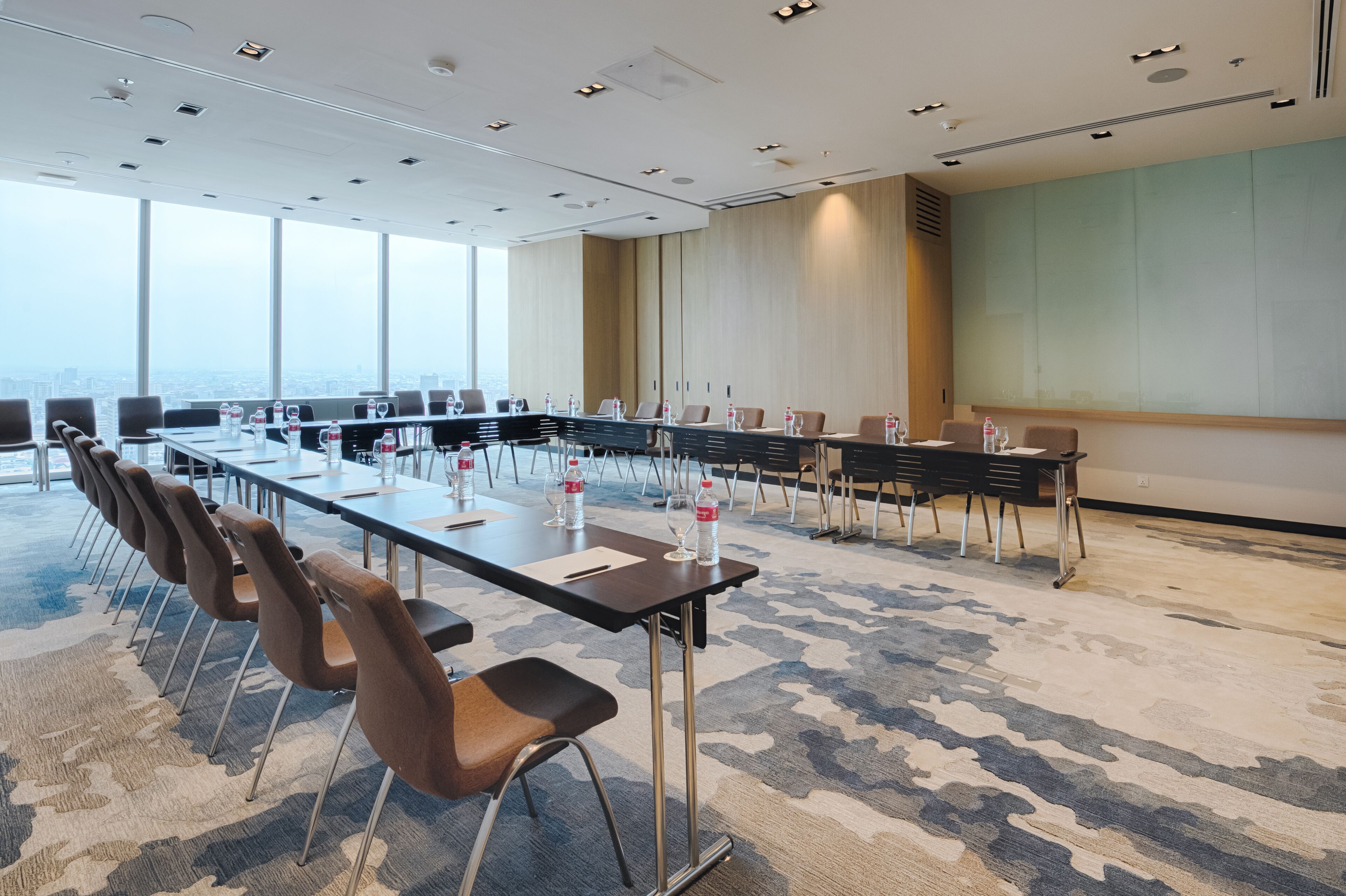 Un salón de conferencias con una mesa larga, sillas y botellas de agua.