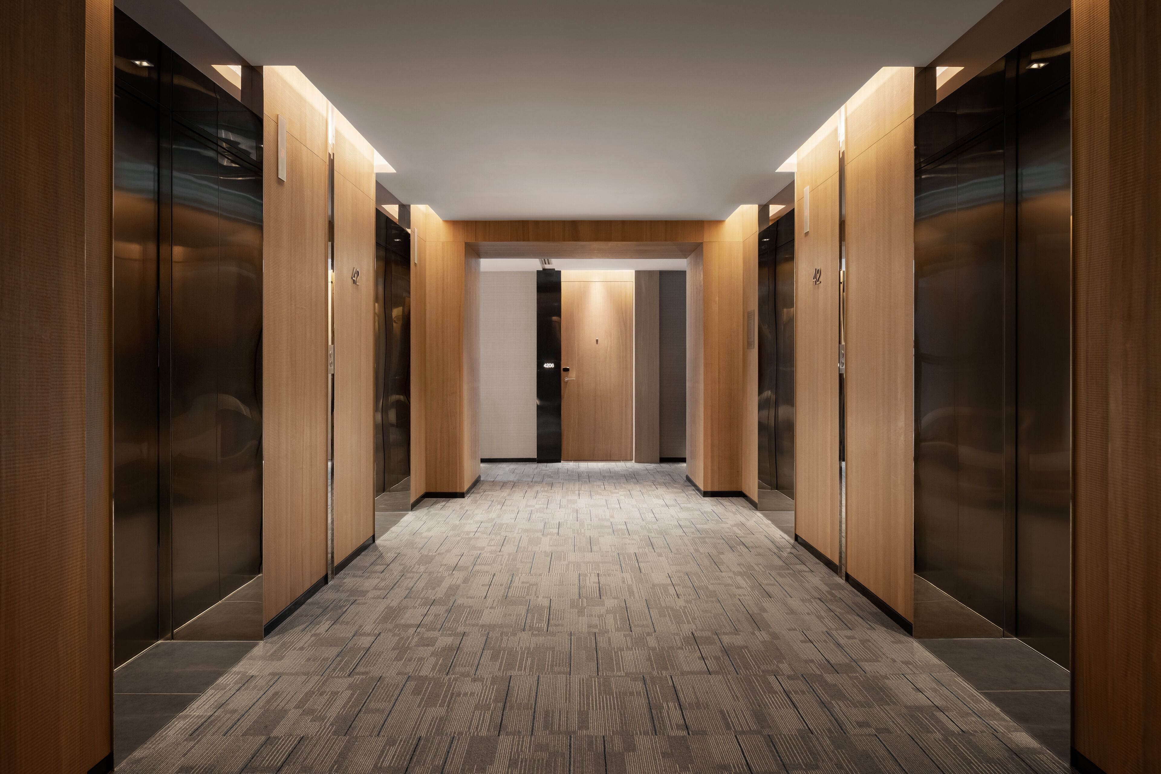 A corridor with wooden walls and a patterned floor, leading to elevators.