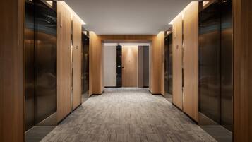 A corridor with wooden walls and a patterned floor, leading to elevators.