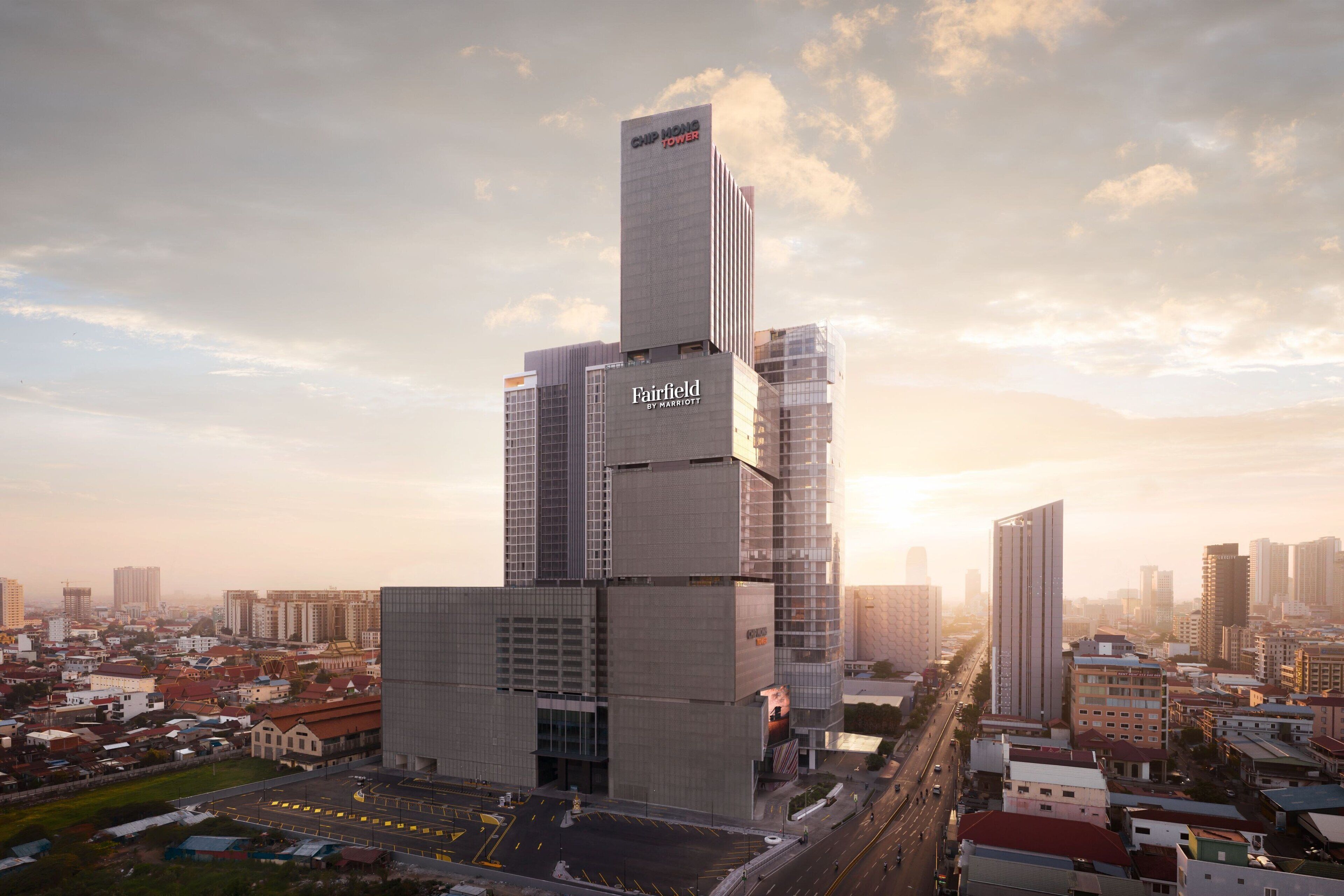 Een modern hotel met een opvallend Fairfield by Marriott bord, omringd door andere hoogbouw en een heldere lucht.