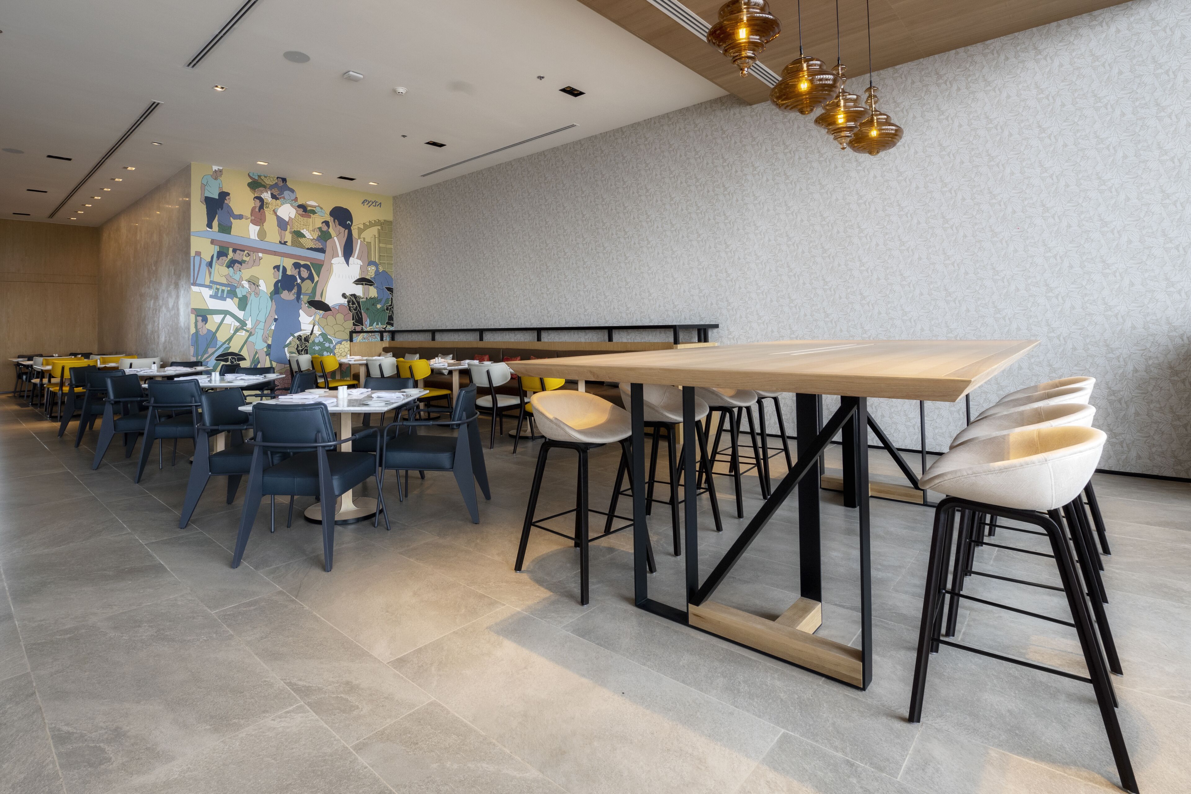 A modern restaurant with high tables and chairs, a mural on the wall, and pendant lighting.