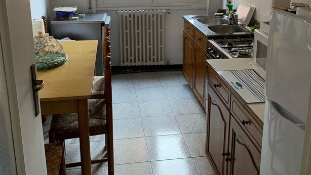 A compact kitchen with wooden cabinets, a dining table with chairs, a window with a view of buildings, and a radiator. - CRÊUZA DE MÄ - nice apartment with convenient parking space by the sea (Rapallo)