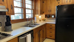 A kitchen with wooden cabinets, a stainless steel sink, a black refrigerator, and a dish rack with utensils. - 2.0 to the Masters! (Augusta)