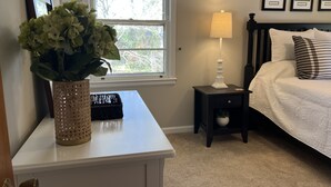 A bedroom with a bed, a bedside table with a lamp, a vase with flowers, and a framed picture on the wall. - 2.0 to the Masters! (Augusta)