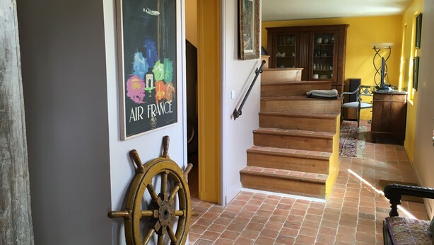 Una scala conduce al secondo piano, con ringhiera in legno e una ruota di timone appesa al muro.