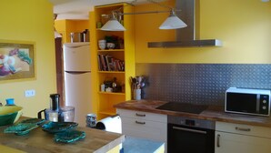 Una cucina con pareti gialle, un forno a microonde, un fornello e un lavello. Si notano delle mensole con libri e utensili da cucina.