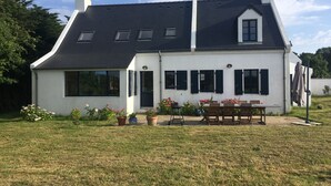 Una casa bianca con tetto scuro, diverse finestre e un patio con tavolo e sedie.