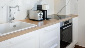 A modern kitchen with white cabinetry, a marble backsplash, a built-in oven, and a coffee maker on the countertop. - Deluxe Apartment (Thasos)