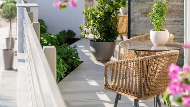 An outdoor patio with wicker chairs and a table, surrounded by potted plants and a stone wall. - Deluxe Apartment (Thasos)