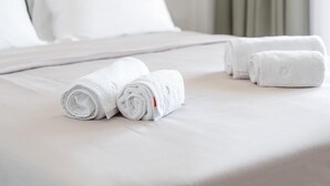 A neatly made bed with white linens and pillows, a grey headboard, and a green curtain. - Premium Apartment (Thasos)