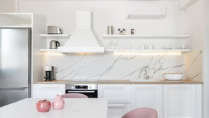 A modern kitchen with white cabinetry, a marble backsplash, and a central island with a pink chair. - Premium Apartment (Thasos)