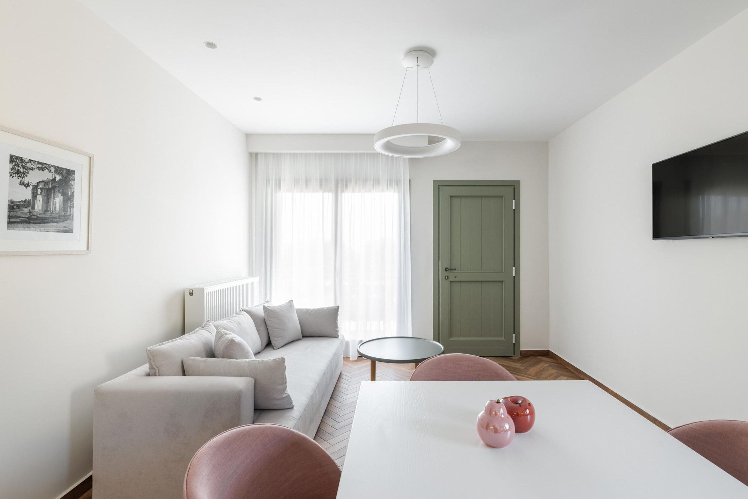 Ein modernes Wohnzimmer mit einer Couch, einem Esstisch mit Stühlen, einem an der Wand montierten Fernseher und einer Tür.