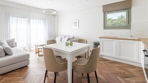 A modern living room with a sofa, dining table, and chairs. There is a kitchen area with a window and a sink. - Superior Apartment (Thasos)
