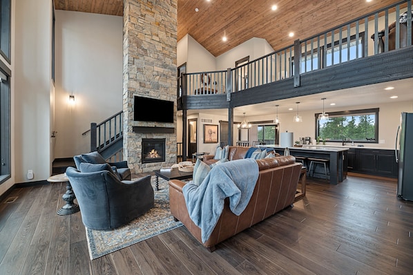 A spacious living area with a stone fireplace, a high ceiling, and a mezzanine level.
