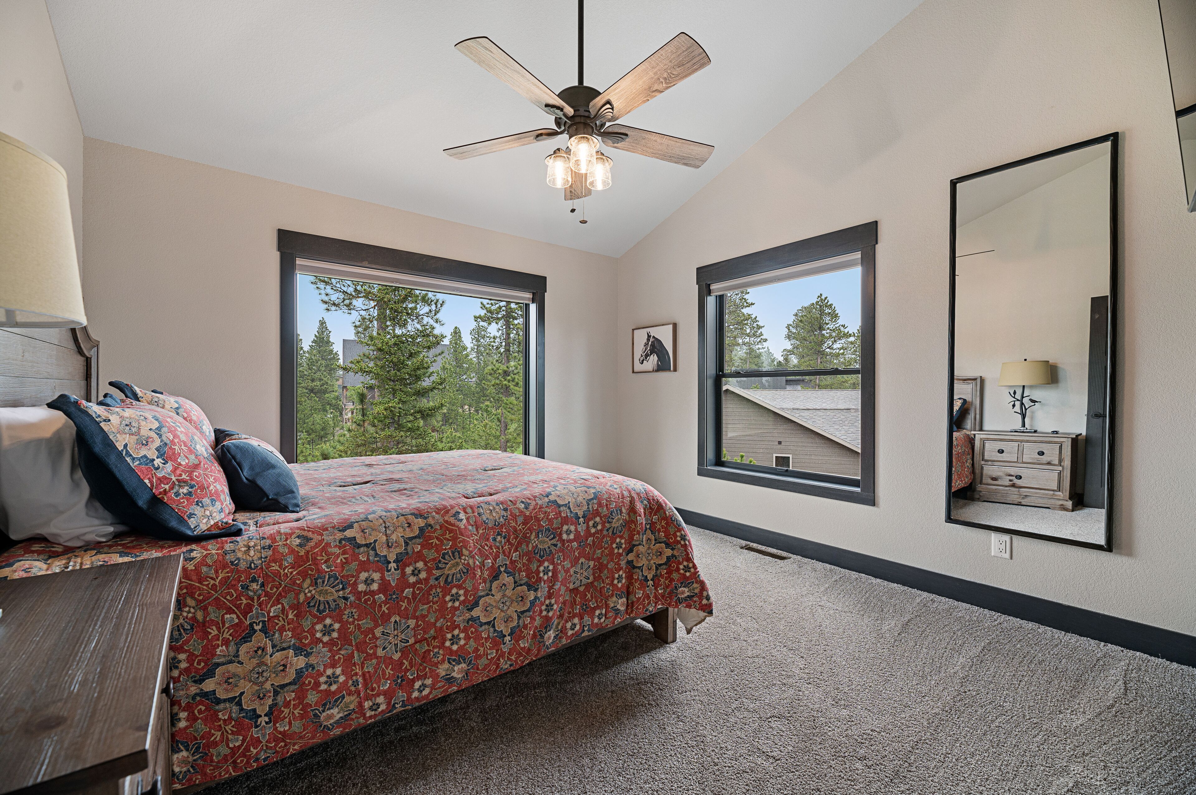 A bedroom with a bed, a ceiling fan, two windows, a dresser, and a mirror.