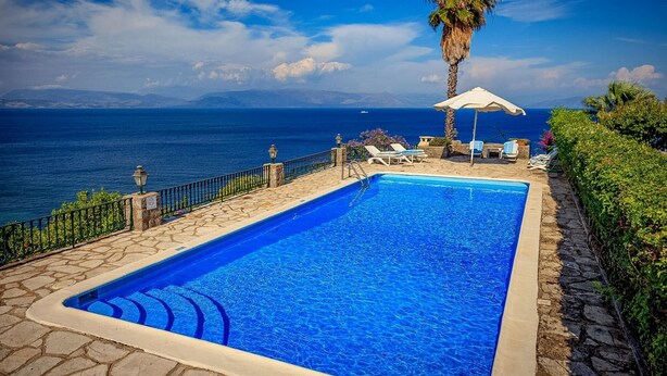 Une piscine rectangulaire bordée de pierres, entourée de chaises longues et d’un parasol, d’où l’on peut admirer un plan d’eau avec des montagnes à l’horizon.
