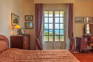 Une chambre à coucher avec un grand lit, une commode, un miroir et une fenêtre avec des rideaux.