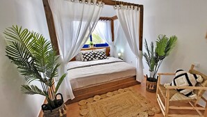 Une chambre à coucher avec un lit, une chaise en bois et deux plantes en pot.