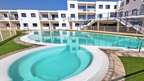 Une piscine au design incurvé, entourée d’une pelouse bien entretenue et d’un bâtiment doté de nombreux balcons et d’escaliers.