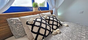 Un lit avec une literie à motifs, une tête de lit en bois et une fenêtre avec des rideaux.