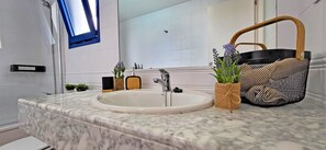 Une salle de bain avec un lavabo en marbre, une petite fenêtre et un panier rempli de plantes.