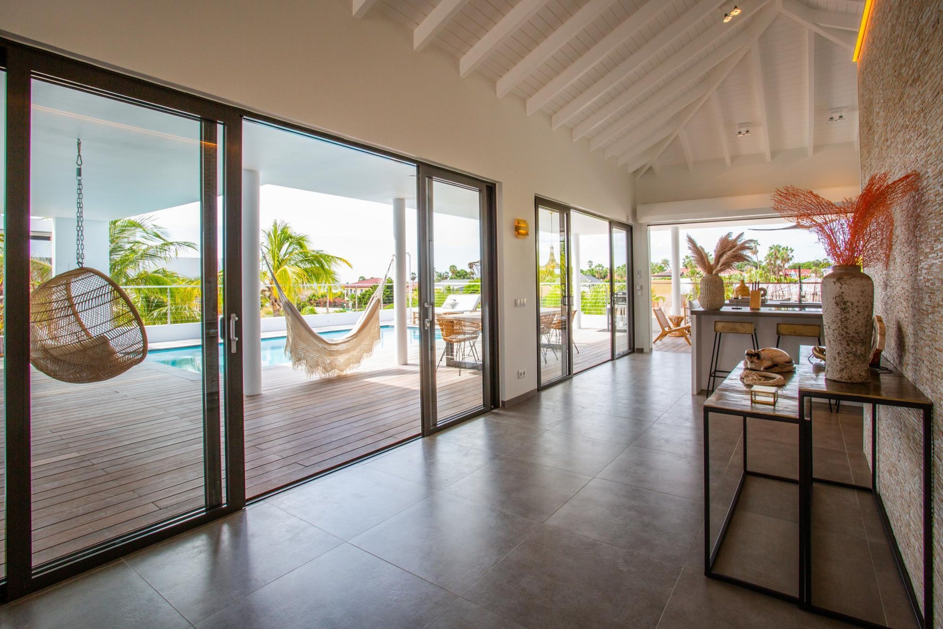 A spacious indoor area with large sliding glass doors leading to a pool area, featuring a hammock and outdoor furniture.
