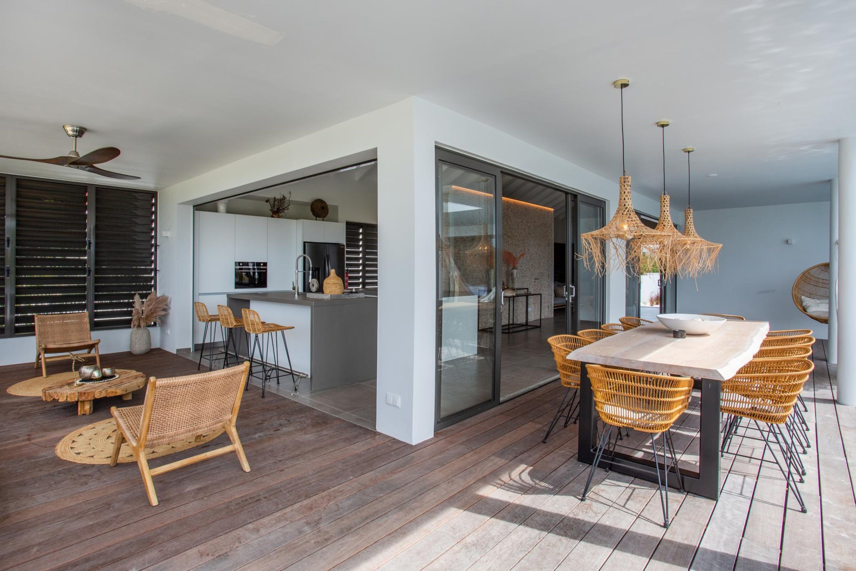 Een moderne keuken met een groot eiland, een eetgedeelte met rieten stoelen en een plafondventilator.