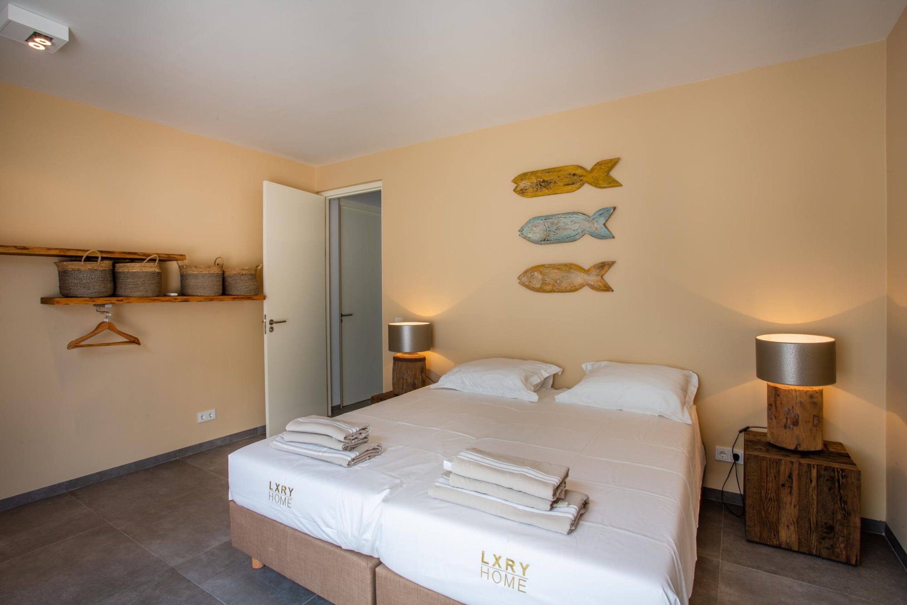 A neatly made bed with folded towels, a wooden nightstand with a lamp, and decorative fish wall art.
