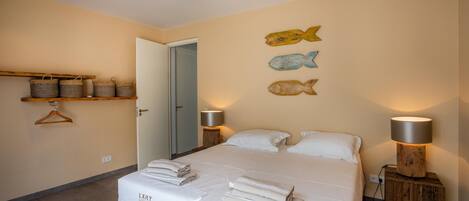 A neatly made bed with folded towels, a wooden nightstand with a lamp, and decorative fish wall art.