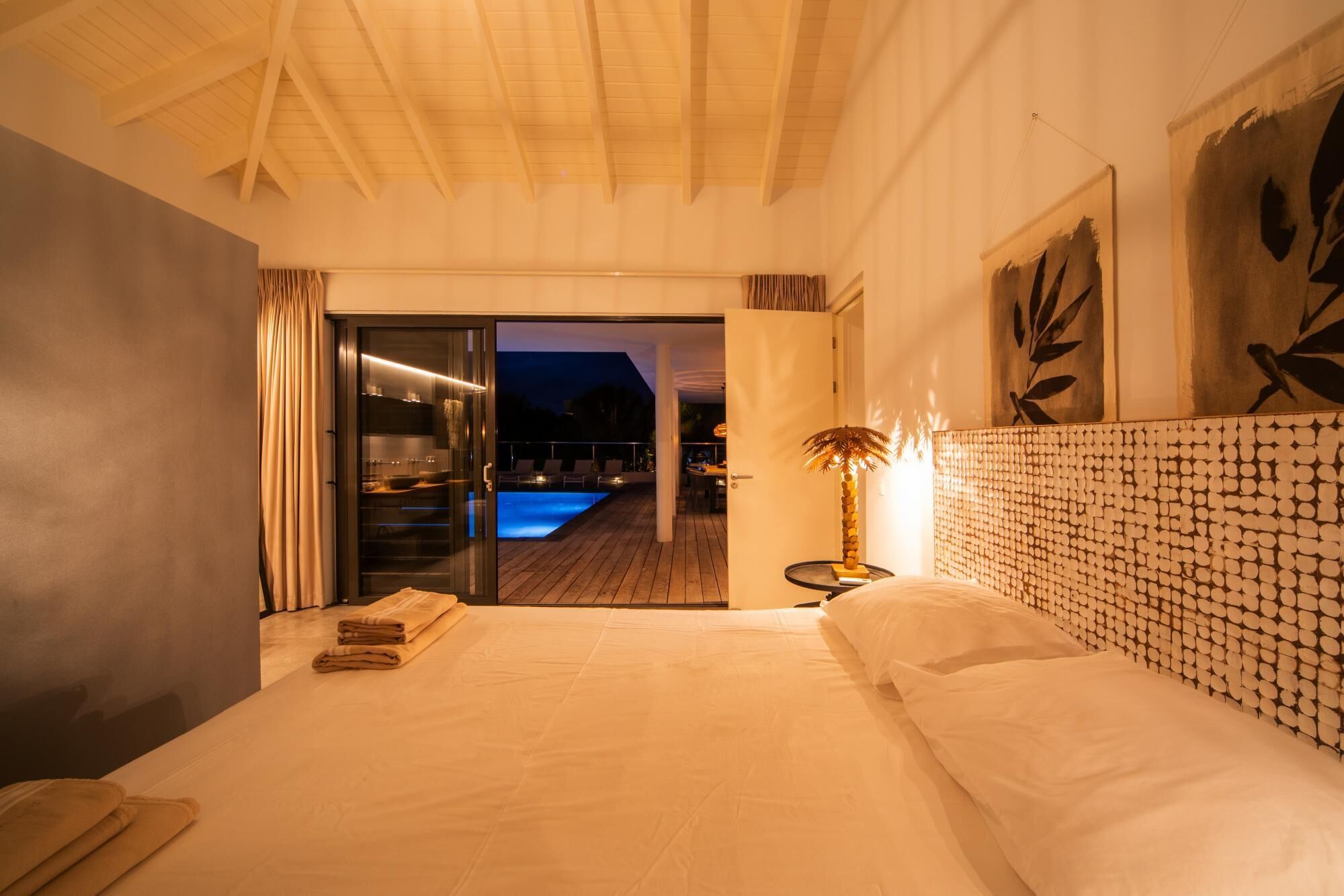 Camera d'albergo con un letto, un comodino, una lampada, vista su una piscina all'aperto e una porta scorrevole che dà su un balcone.